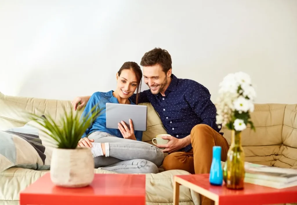 casal sentado no sofá enquanto olham algo no notebook