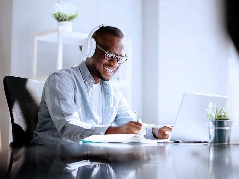 Homem feliz usando fones de ouvido trabalhando no computador.