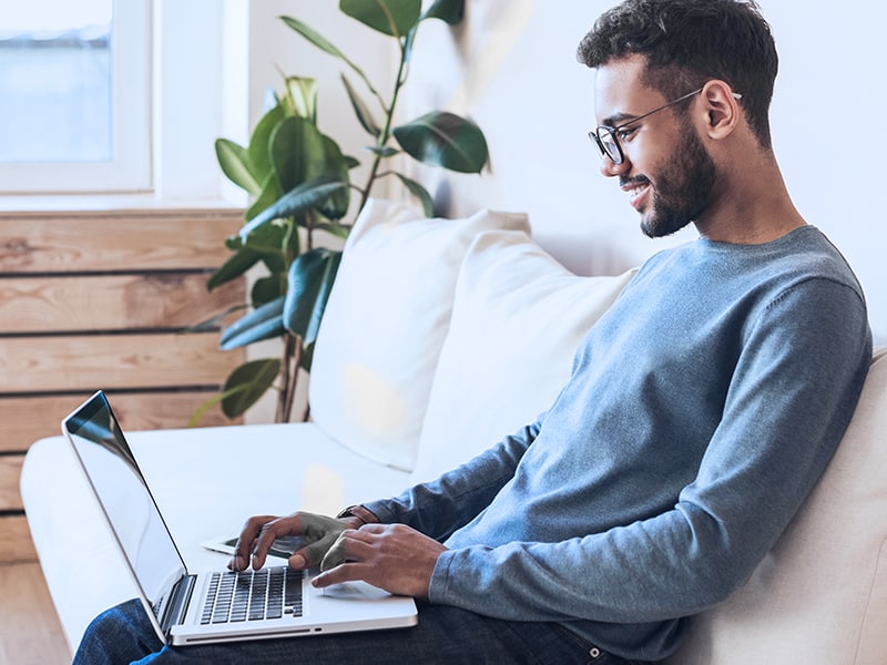 Homem sentado em um sofá com notebook sobre o colo