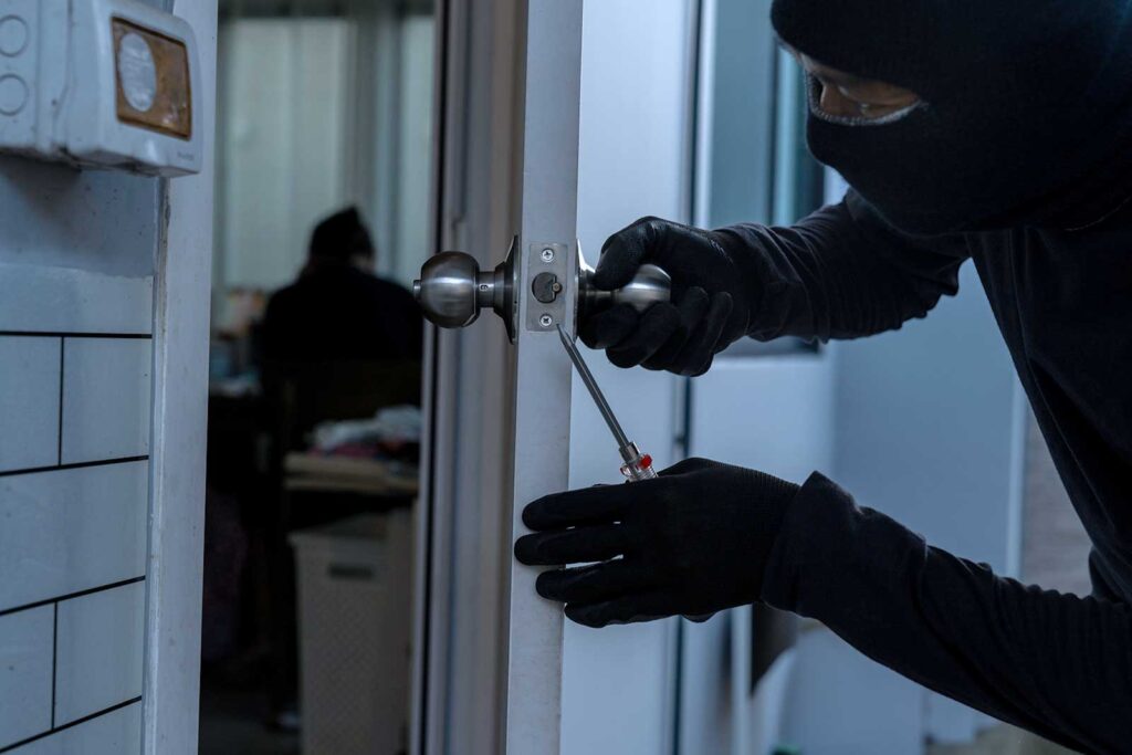 Ladrão encapuzado usando uma chave de fenda para arrombar uma maçaneta de porta em um escritório.