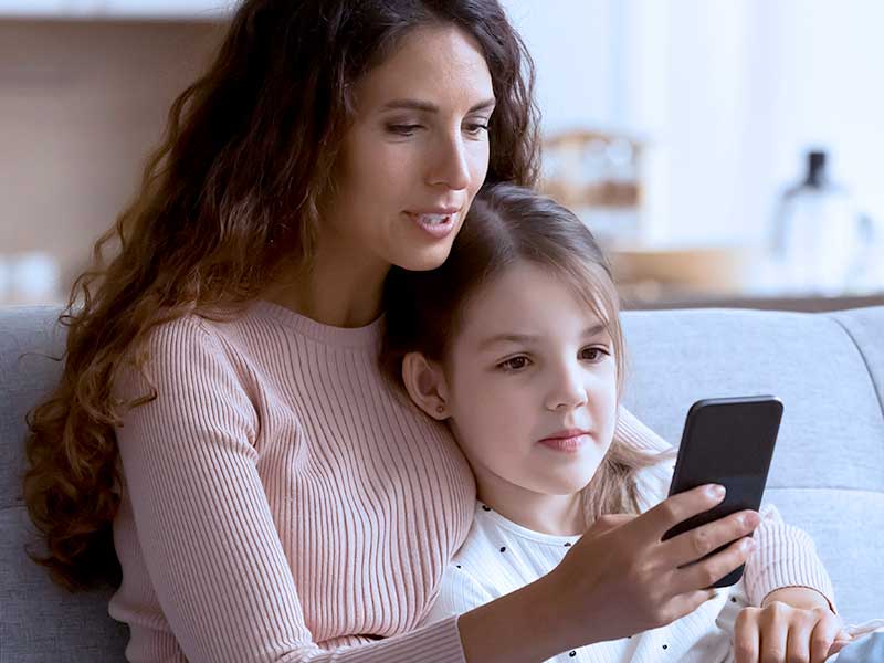 Mãe e filha usando celular juntas no sofá