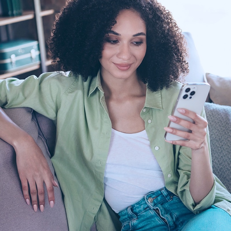Mulher sentada no sofá segurando celular na mão.