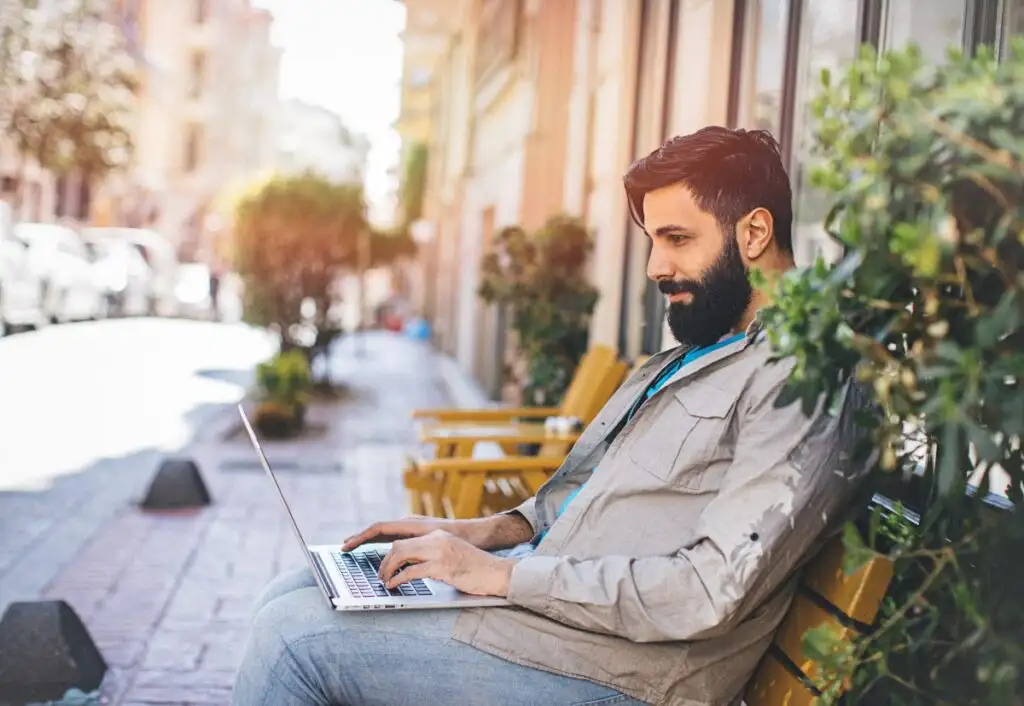 homem sentado em um banco da rua usando seu notebook