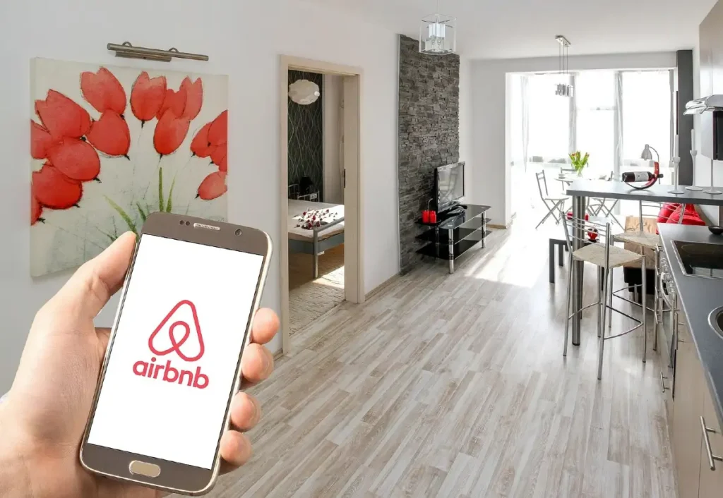 homem dentro de uma segurando um celular na mão com a logo do airbnb na tela