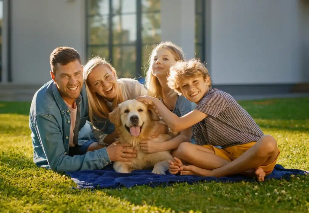 família de 4 pessoas e um cachorro, sentados e abraçados na grama de casa