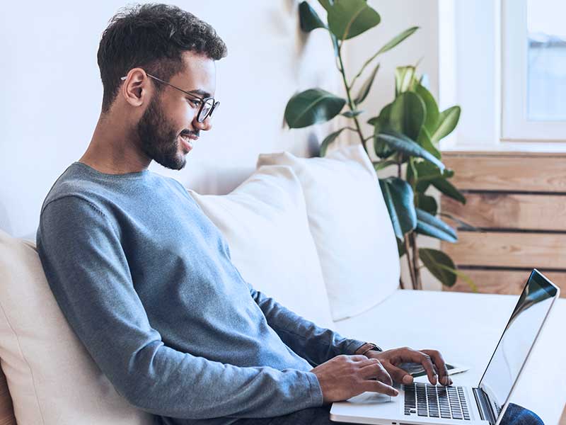Homem sentado no sofá mexendo no notebook.
