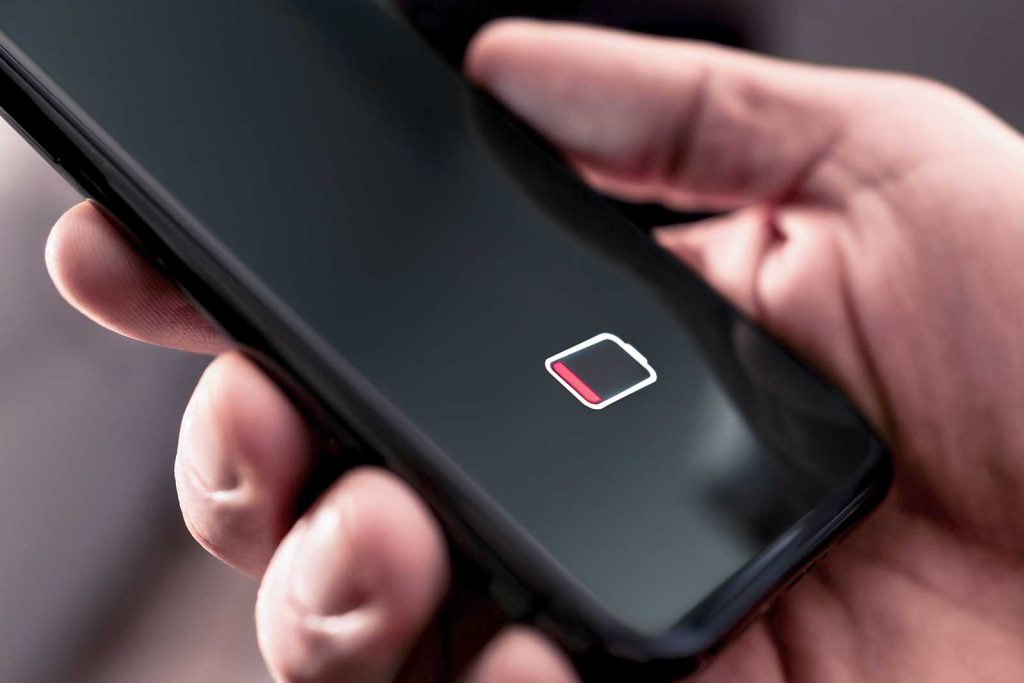 Mão segurando celular com ícone de bateria baixa
