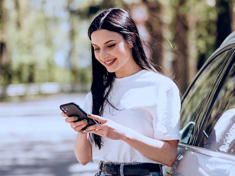 Jovem mulher sorrindo enquanto usa o celular ao ar livre