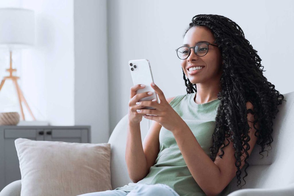Mulher sorrindo enquanto usa smartphone em casa.