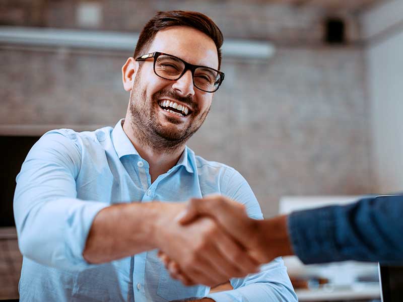Homem sorrindo enquanto aperta mãos em escritório.