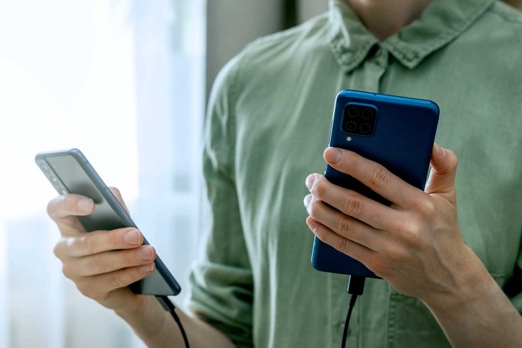 Pessoa segurando dois smartphones carregando