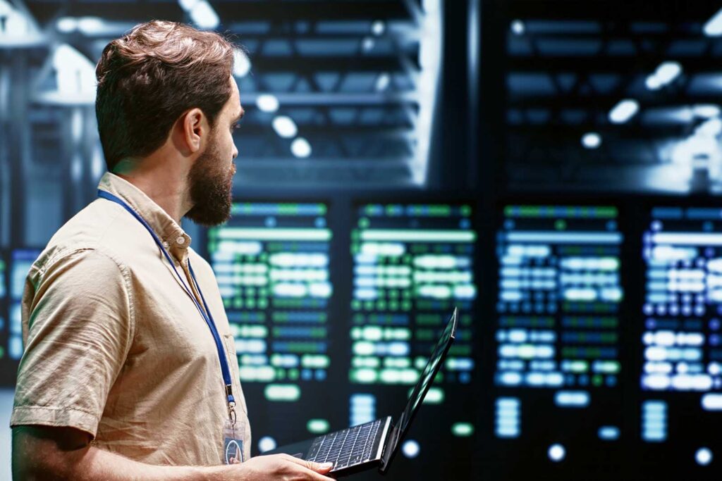 Homem com laptop em frente a telas de dados