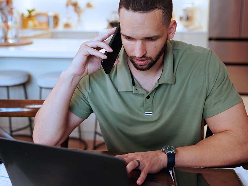 Homem falando ao telefone enquanto trabalha no laptop.