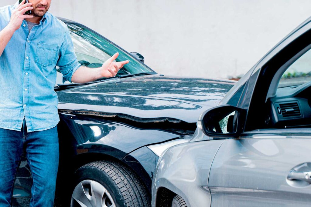 Homem usando celular após batida de carros.