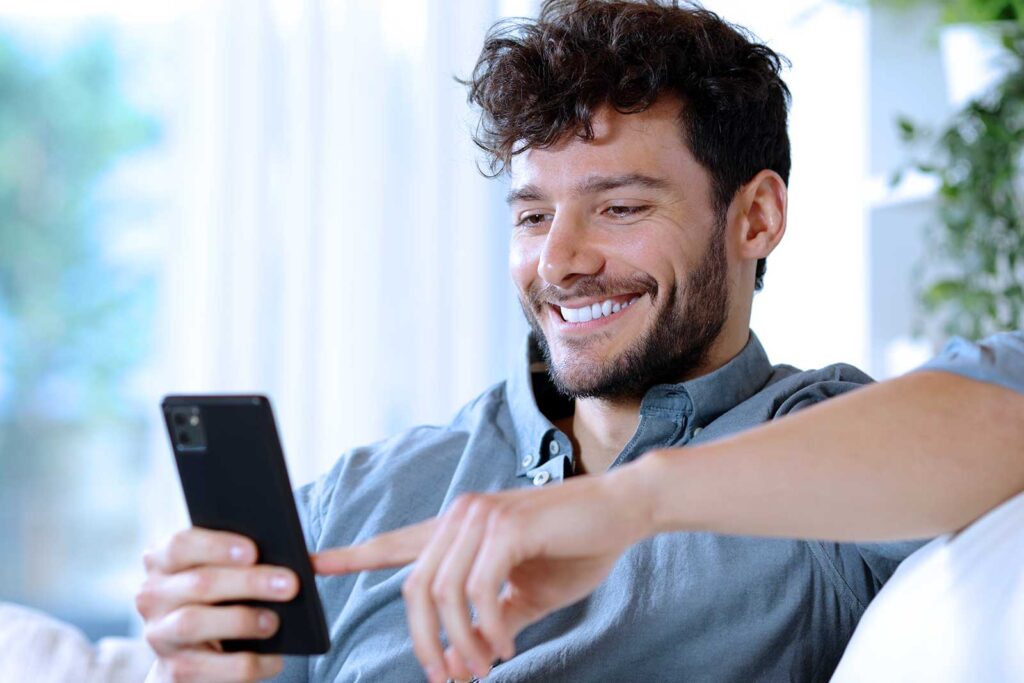 Homem sorrindo usando smartphone em casa