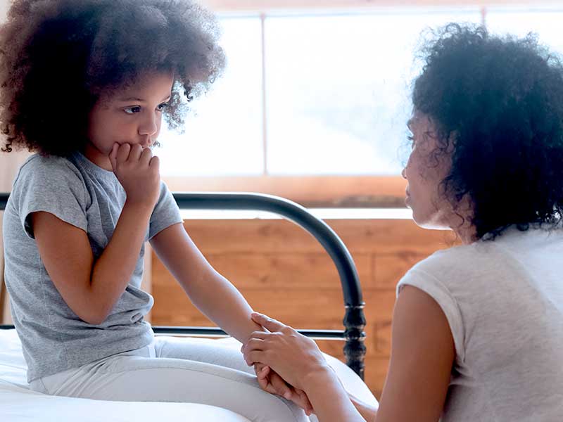 Mãe conversando com filha preocupada na cama