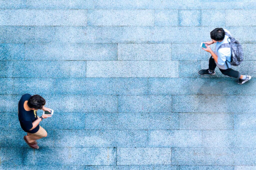 Pessoas caminhando e usando celulares em calçada