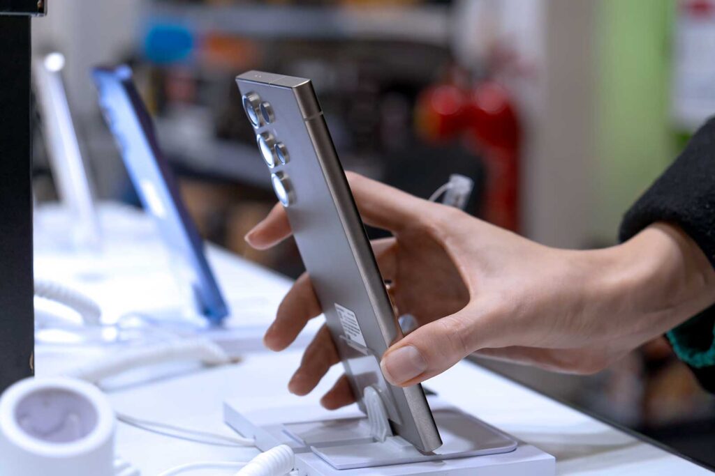 Mão segurando smartphone em loja de eletrônicos