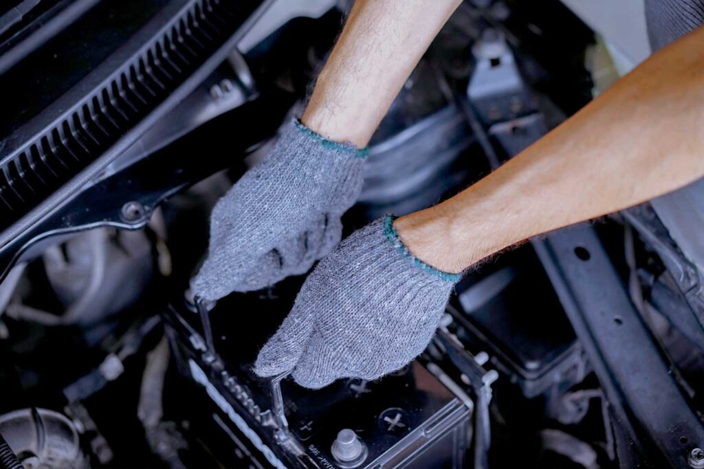 Pessoa trocando bateria de carro com luvas