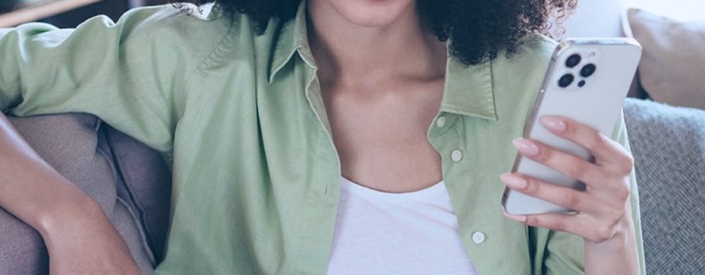 Mulher sentada no sofá segurando celular na mão.