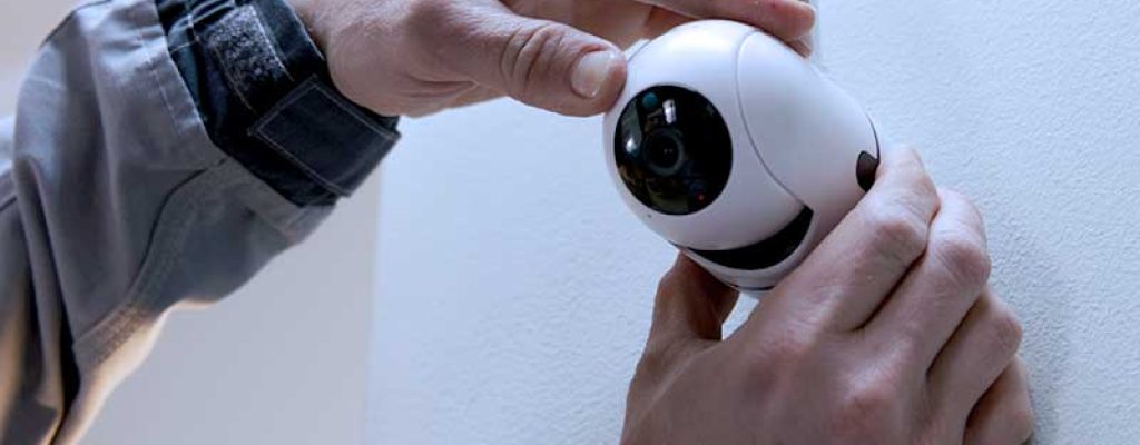 Close-up das mãos de uma pessoa instalando uma câmera de segurança sem fio branca na parede.