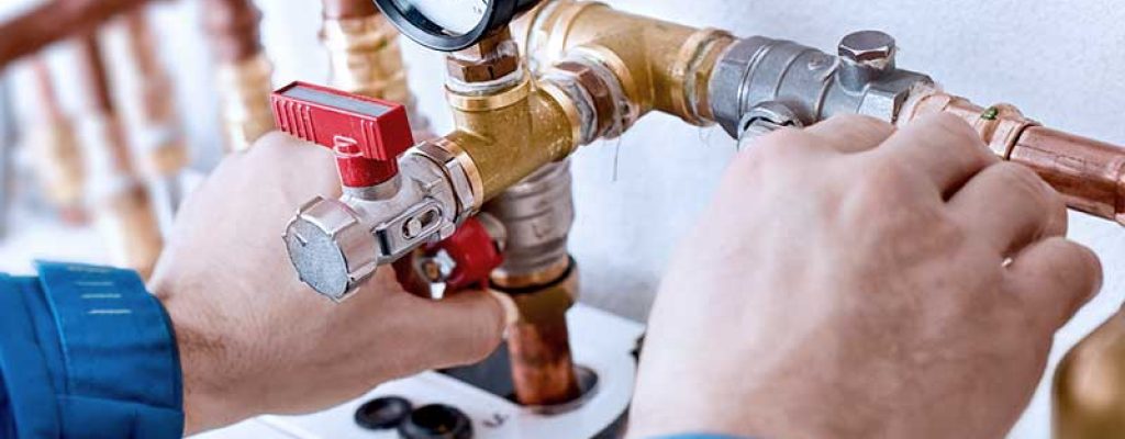 Mãos de um encanador ajustando válvulas e manômetro em um sistema de encanamento de cobre.
