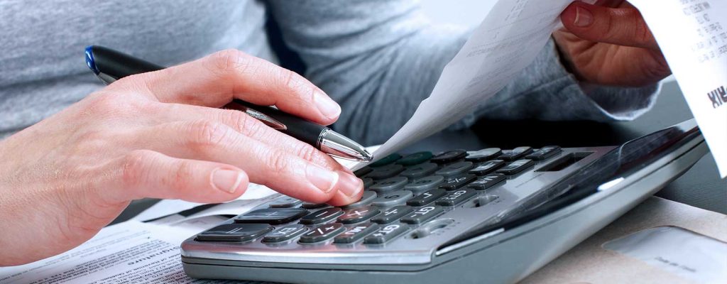 Uma pessoa fazendo cálculo em uma calculadora segurando uma nota fiscal.