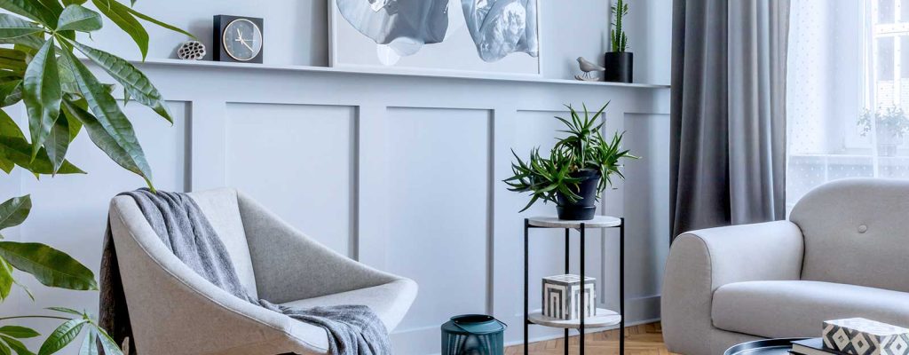 Sala de estar moderna com poltrona cinza, sofá, plantas, mesa de centro e quadro abstrato na parede. Piso de madeira clara e cortinas cinza.