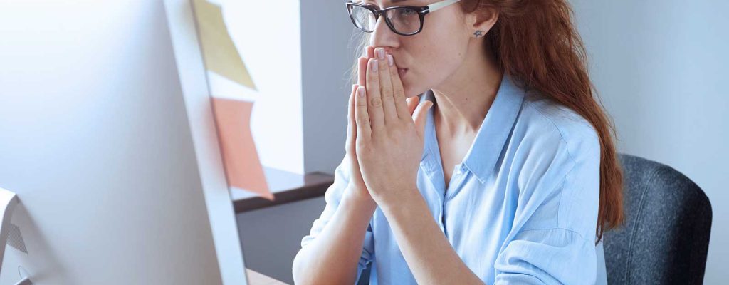 Mulher sentada a frente de um computador com as mãos juntas.