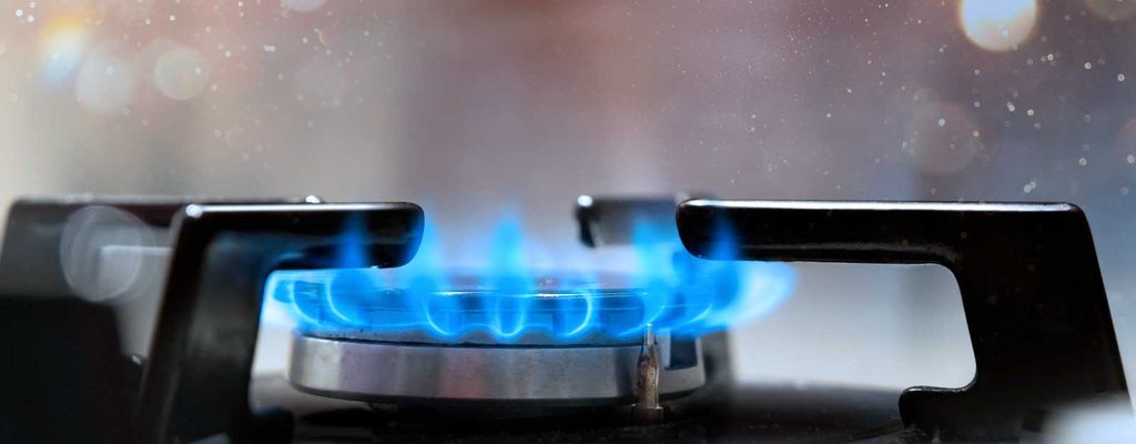 Chama azul vibrante de um fogão a gás aceso, com um fundo desfocado de luzes brilhantes.