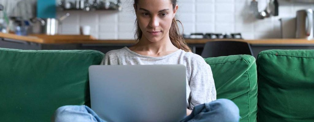 Mulher sentada no sofá mexendo no computador.