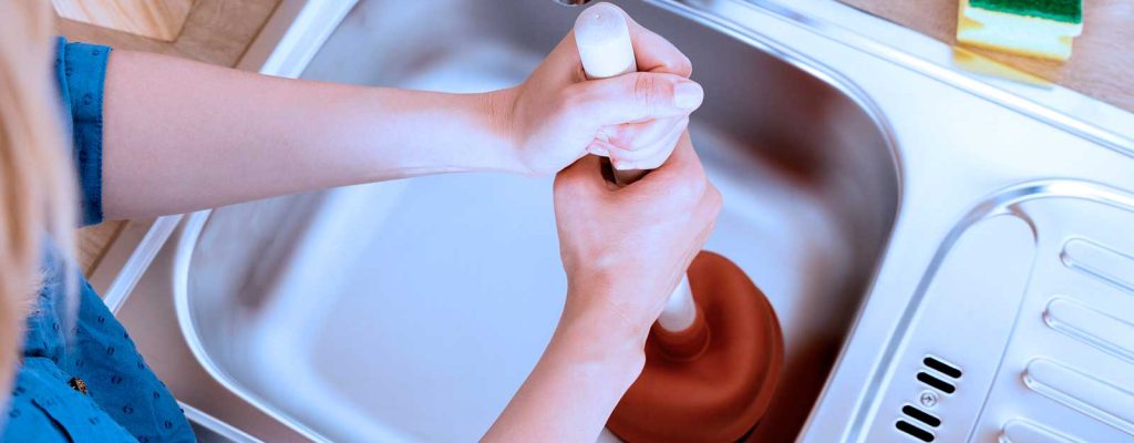 Pessoa desentupindo pia da cozinha com desentupidor
