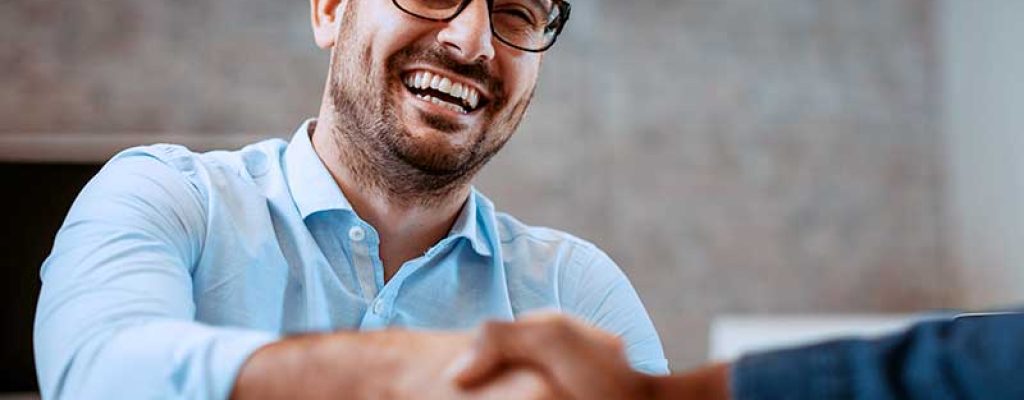 Homem sorrindo enquanto aperta mãos em escritório.