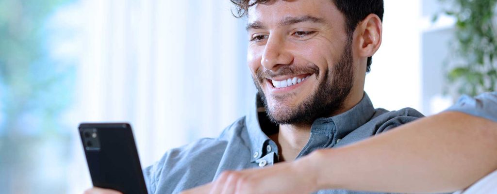 Homem sorrindo usando smartphone em casa