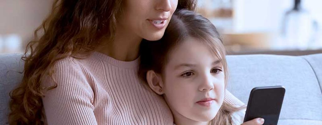 Mãe e filha usando celular juntas no sofá